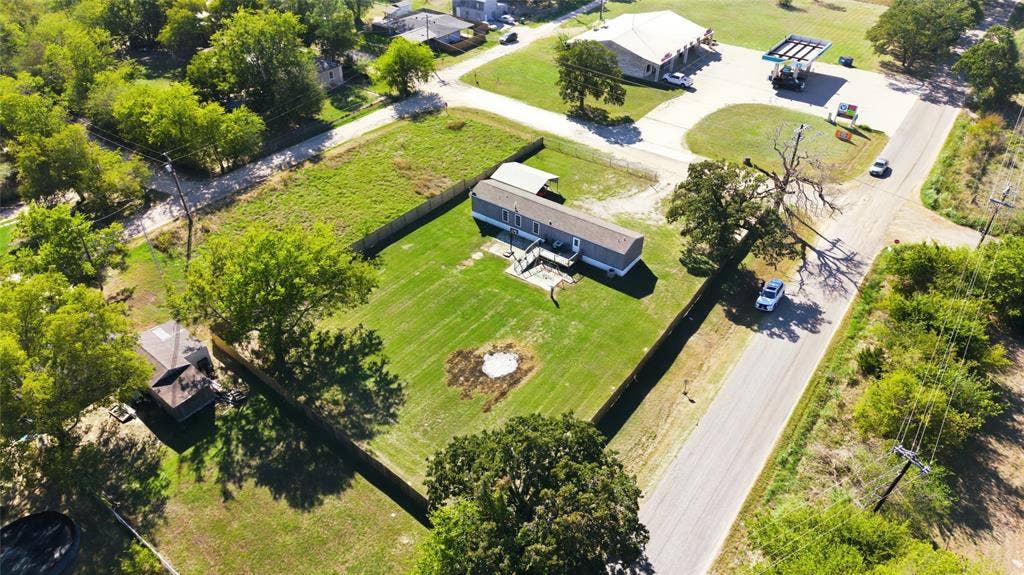 Aerial perspective of a property featuring a fenced perimeter, expansive lawn, detached storage structure, and a covered carport