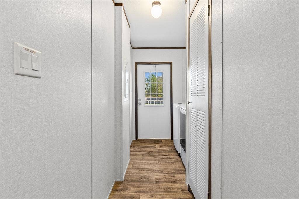 Utility area featuring wood-finish flooring, white panel walls, louvered closet doors, and an exterior door with a multi-pane glass insert