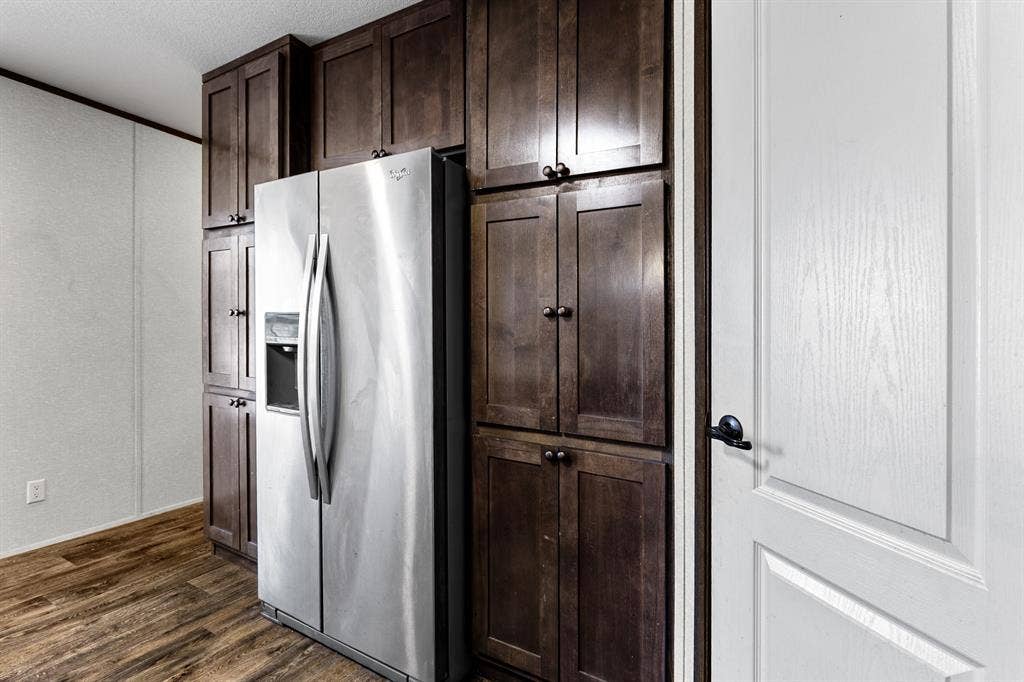 Dark wood-finish cabinetry featuring shaker-style doors, integrated stainless steel refrigerator, and wood-finish flooring