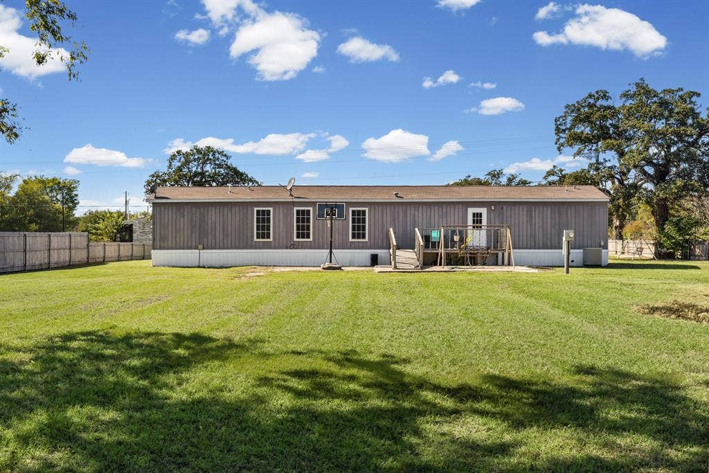 Exterior elevation featuring vertical siding, a raised wooden deck with railings, and a spacious rear lawn enclosed by a perimeter fence
