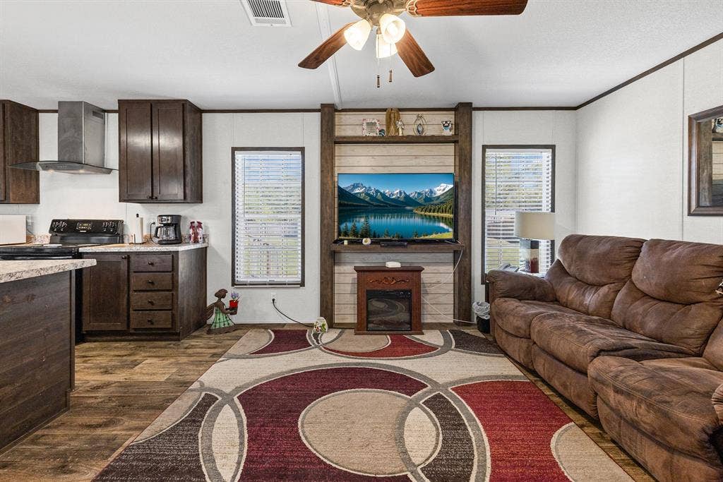 Dark wood cabinetry, wood-finish flooring, built-in entertainment center with shiplap accent, and ceiling fan with light fixture