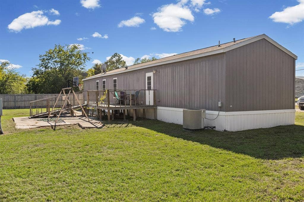 Exterior profile featuring vertical panel siding, a raised wood deck, a concrete patio area, and perimeter wood fencing