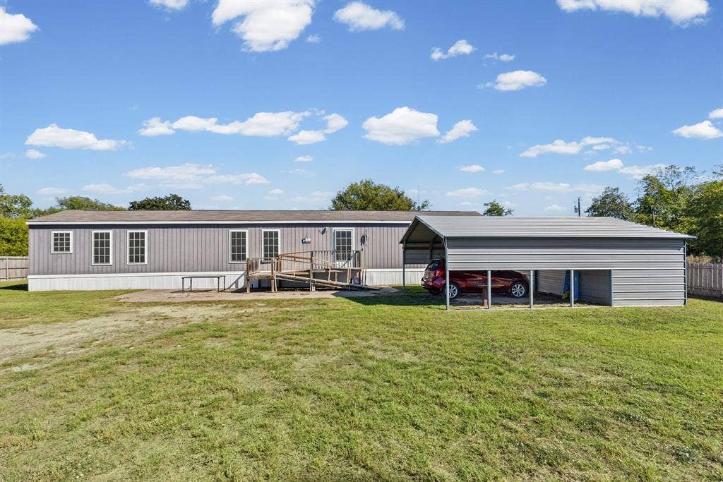 Exterior featuring vertical siding, a metal-roofed carport, a wooden accessibility ramp, and a sprawling lawn
