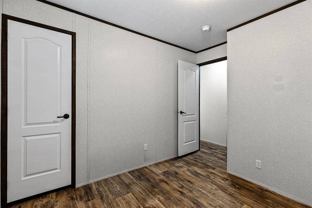 Bedroom space featuring textured wall panels, wood-finish flooring, and white two-panel interior doors with dark hardware and matching trim