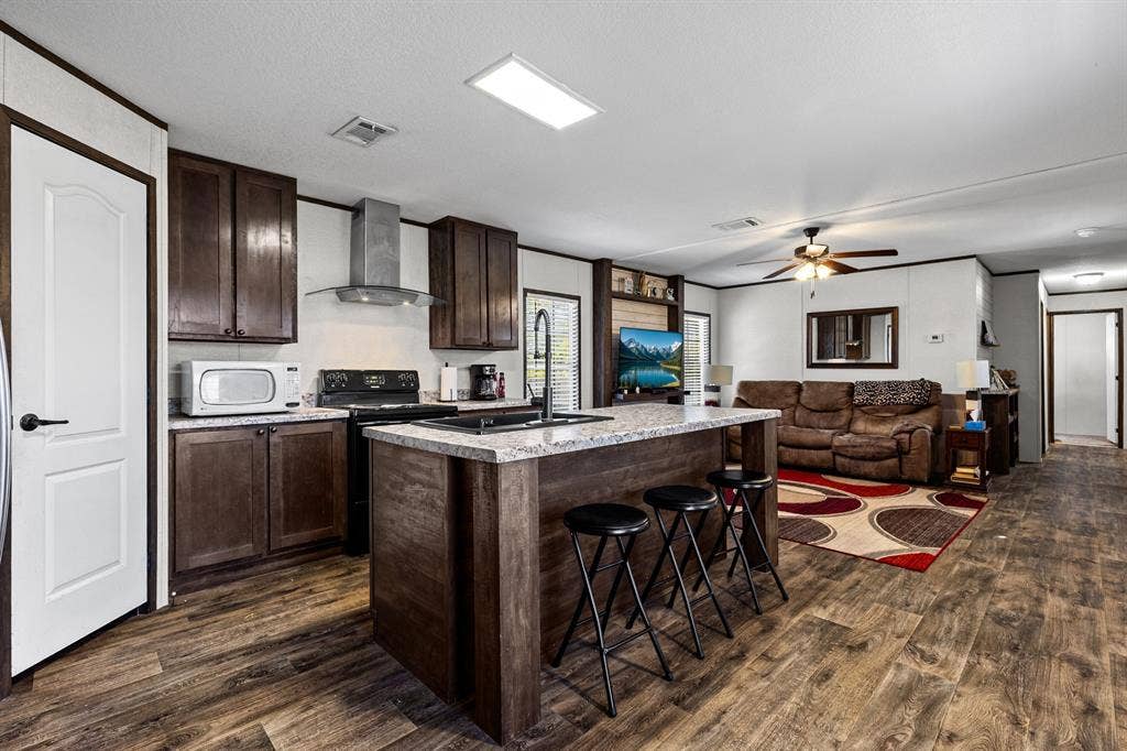 Kitchen featuring dark wood cabinetry, a central island with stone-finish countertops, and a stainless steel wall-mounted range hood, complemented by wood-finish flooring
