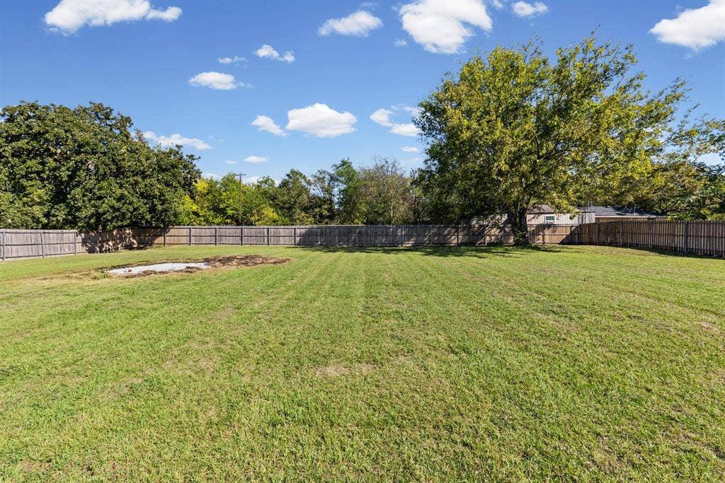 Expansive backyard featuring a large grass lawn, perimeter wood fencing, and mature trees