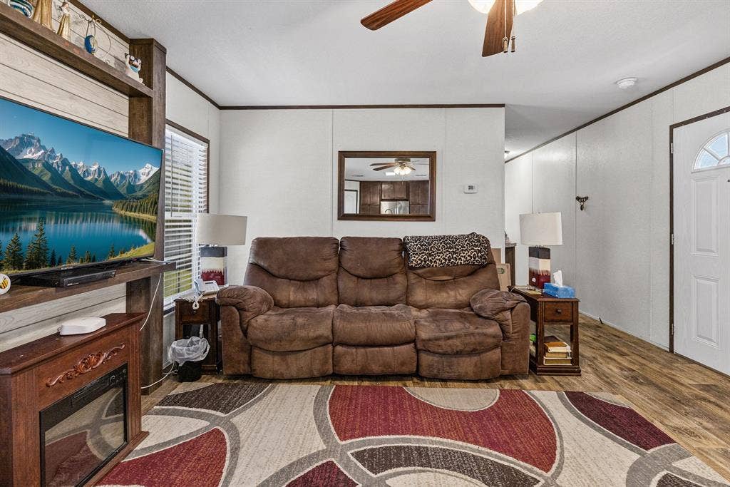 Living area featuring wood-finish flooring, a ceiling fan with integrated lighting, and a built-in entertainment center with a fireplace insert
