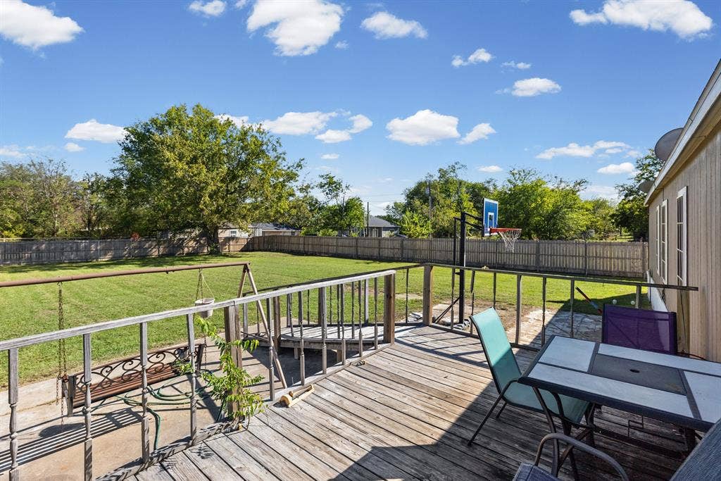 Elevated wooden deck featuring wood railings, concrete patio space, and a fenced-in backyard with mature trees