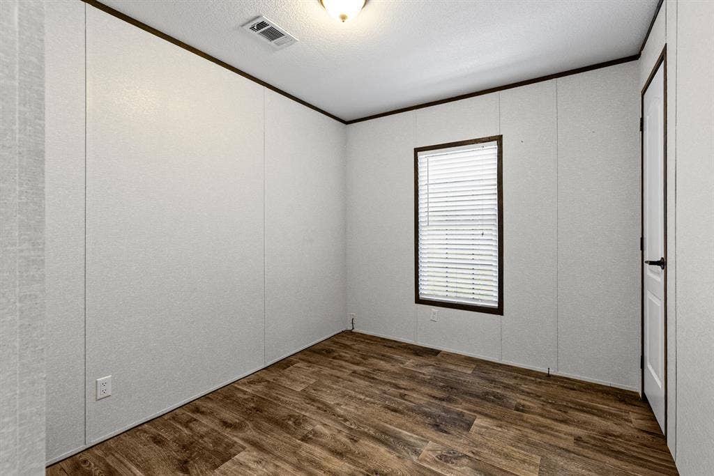 Bedroom featuring wood-finish flooring, a single-window configuration with horizontal blinds, neutral panel walls, dark trim, and a ceiling-mounted light fixture
