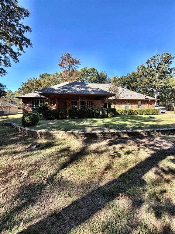 9031 Mallard Way, Larue, TX 75770 Brick exterior residence featuring a covered front porch, stone retaining wall, and mature trees on the surrounding lot
