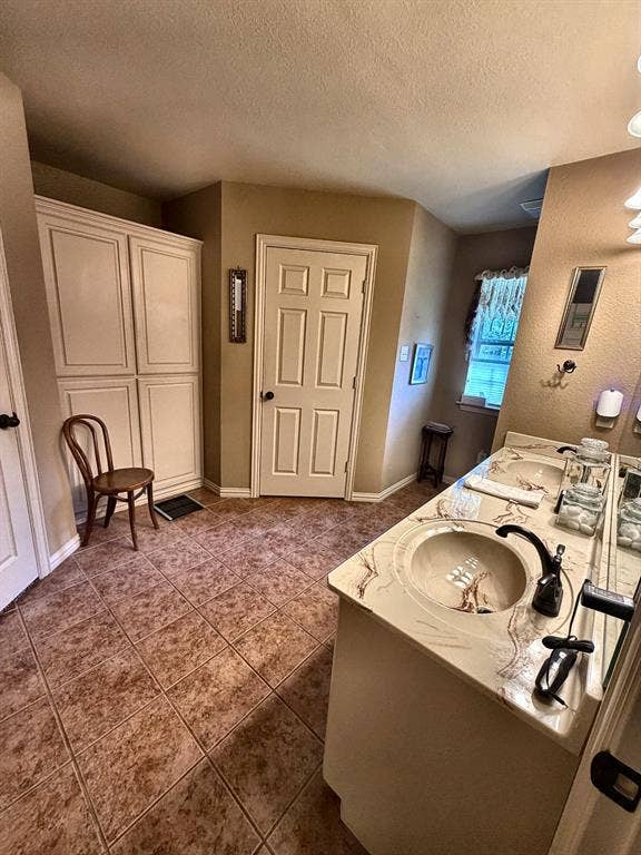 9031 Mallard Way, Larue, TX 75770 Bathroom featuring dual-sink vanity with patterned stone-finish countertop, tile flooring, built-in floor-to-ceiling storage cabinetry, and multi-light vanity fixture