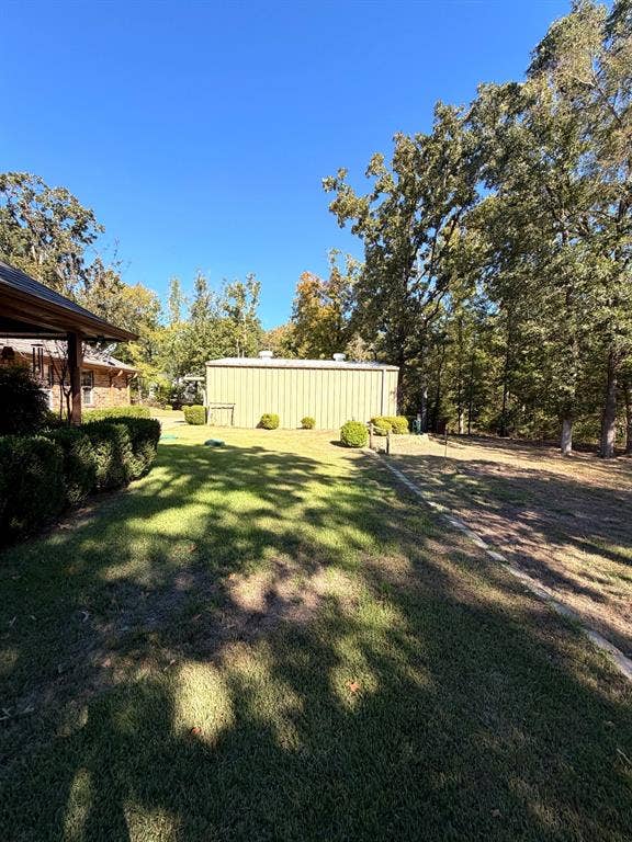 9031 Mallard Way, Larue, TX 75770 Expansive backyard featuring a metal detached structure, manicured grass, mature trees, and tiered landscaping