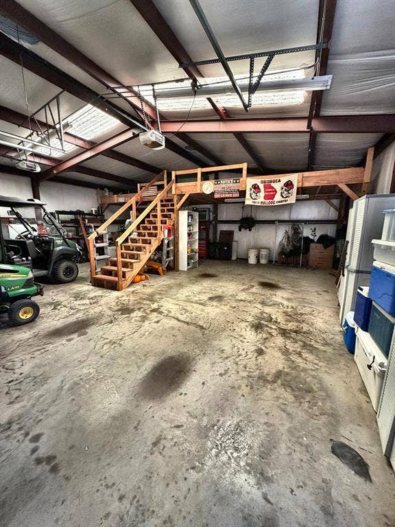 9031 Mallard Way, Larue, TX 75770 Spacious workshop featuring a concrete floor, exposed steel beams, translucent roof panels, and an elevated wooden loft with a built-in staircase