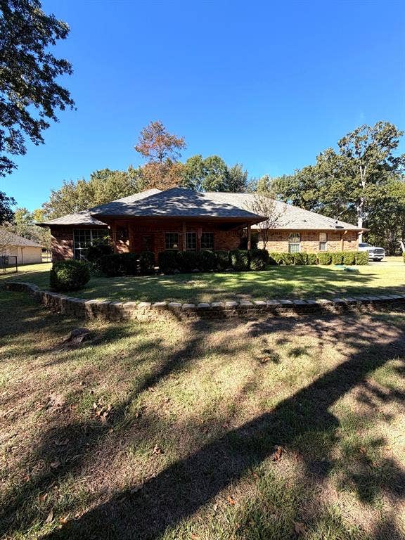 9031 Mallard Way, Larue, TX 75770 Single-story brick exterior featuring a covered front porch, tiered natural stone retaining wall, and mature landscaping