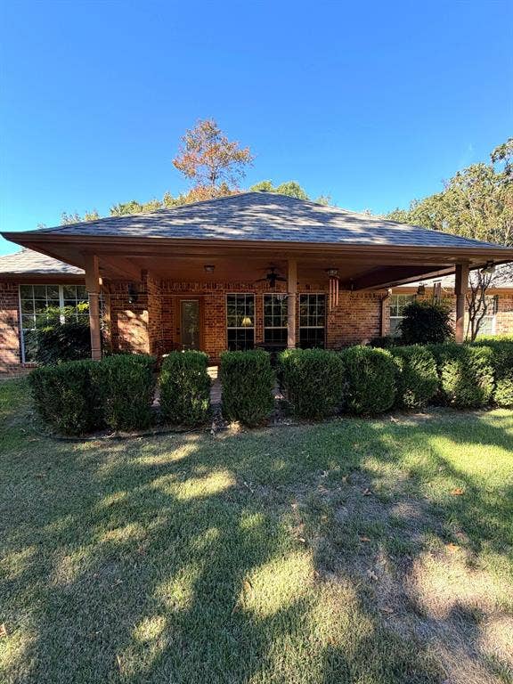 9031 Mallard Way, Larue, TX 75770 Brick exterior featuring a covered patio, hipped roofline, multiple windows, and a manicured lawn
