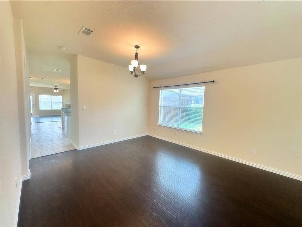 Spare room featuring ceiling fan with notable chandelier, plenty of natural light, and dark hardwood / wood-style flooring