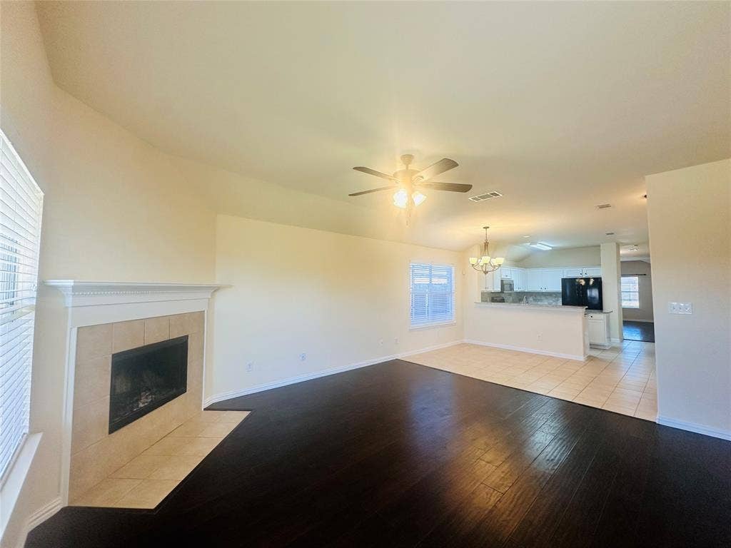 Unfurnished living room featuring lofted ceiling, a tiled fireplace, ceiling fan with notable chandelier, and light wood-type flooring