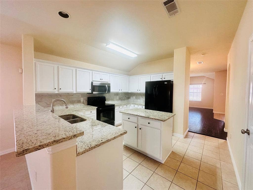 Kitchen with light stone counters, a center island, sink, and black appliances