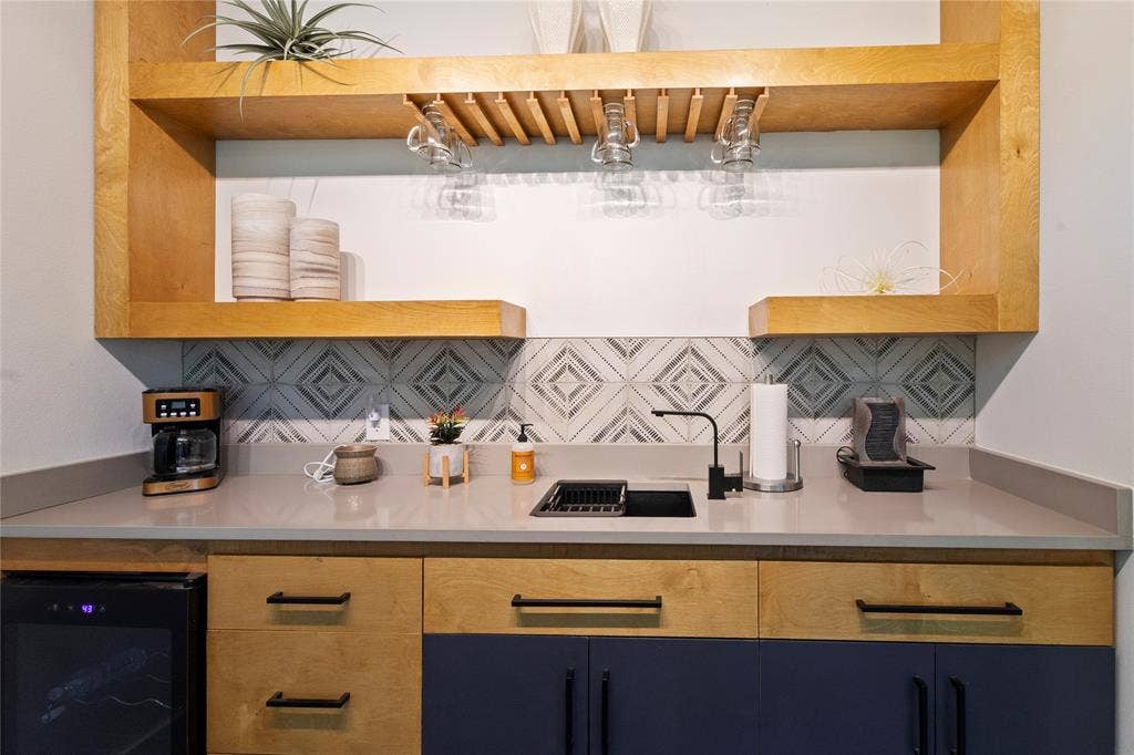 6113 Ottawa Trail, Mabank, TX 75156 Built-in wet bar featuring custom two-tone cabinetry, solid-surface countertops, decorative tile backsplash, floating wooden shelves with integrated stemware rack, and a dedicated beverage refrigerator