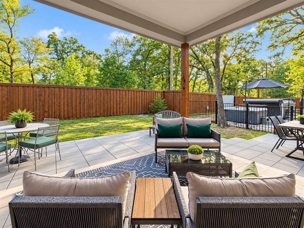 6113 Ottawa Trail, Mabank, TX 75156 Covered patio featuring large-format stone pavers, wood-finished support column, privacy wood fencing, black metal perimeter fencing, and an integrated spa