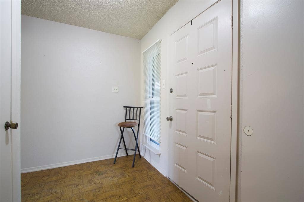 626 Thornwood Trail, Grand Prairie, TX 75052 Entryway featuring parquet wood-finish flooring, a six-panel door with metallic hardware, a vertically oriented window with horizontal blinds, and a textured ceiling