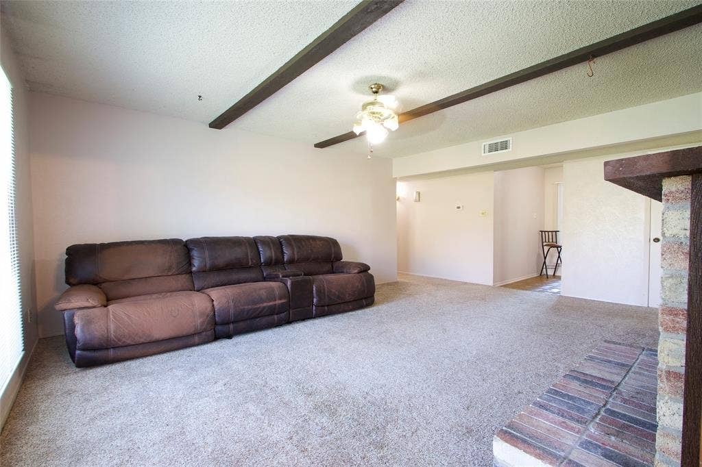 626 Thornwood Trail, Grand Prairie, TX 75052 Living area featuring exposed wooden ceiling beams, a ceiling fan with integrated lighting, and a brick fireplace hearth