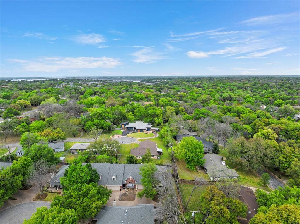 201 Pecan Village Circle, Waco, TX 76710 Aerial perspective of a sprawling residential area featuring extensive tree coverage, winding suburban streets, and multiple homes with pitched rooflines