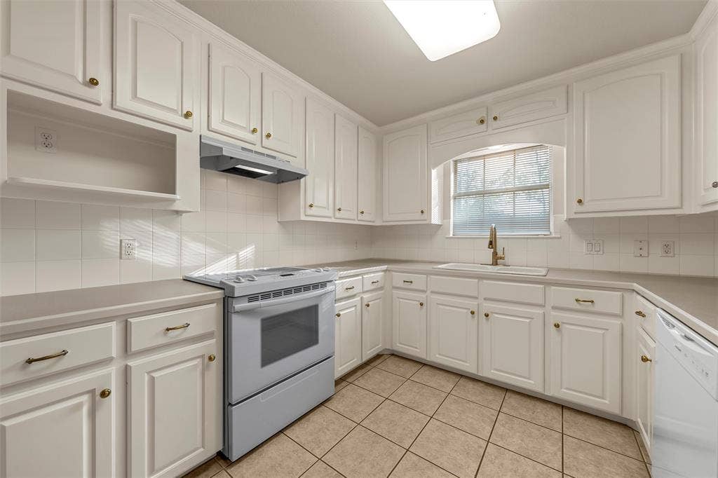 201 Pecan Village Circle, Waco, TX 76710 Kitchen featuring white shaker-style cabinetry, solid surface countertops, ceramic tile backsplash, tiled flooring, and a built-in range hood