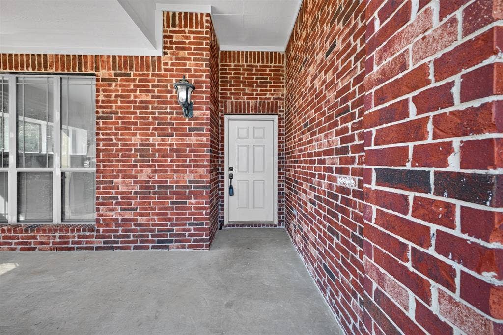 701 Abbey Lane, Midlothian, TX 76065 Covered entrance featuring red brick exterior, multi-pane window, and wall-mounted lantern-style lighting fixture