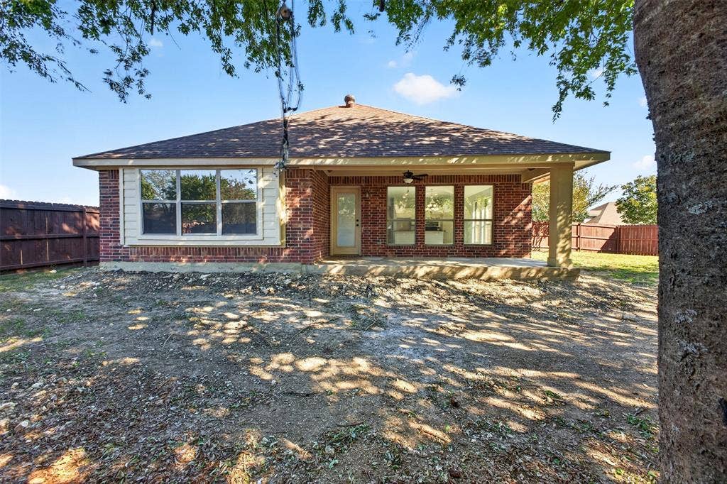 701 Abbey Lane, Midlothian, TX 76065 Brick exterior featuring a covered rear patio, hipped roofline, and wood-style fencing