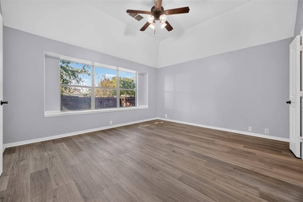 701 Abbey Lane, Midlothian, TX 76065 Vaulted ceiling featuring a central multi-blade ceiling fan with integrated lighting, wood-finish flooring, and expansive windows
