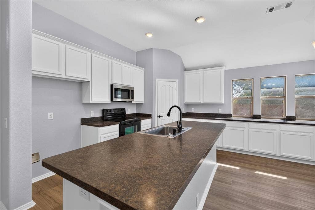 701 Abbey Lane, Midlothian, TX 76065 Kitchen featuring white shaker-style cabinetry, a dark-toned laminate countertop, center island with a stainless steel sink and matte black faucet, and wood-finish flooring
