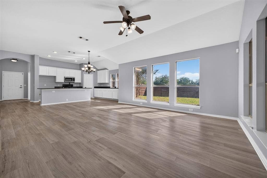 701 Abbey Lane, Midlothian, TX 76065 Open-concept interior featuring vaulted ceilings, wood-finish flooring, a kitchen with white cabinetry, dark countertops, and large windows