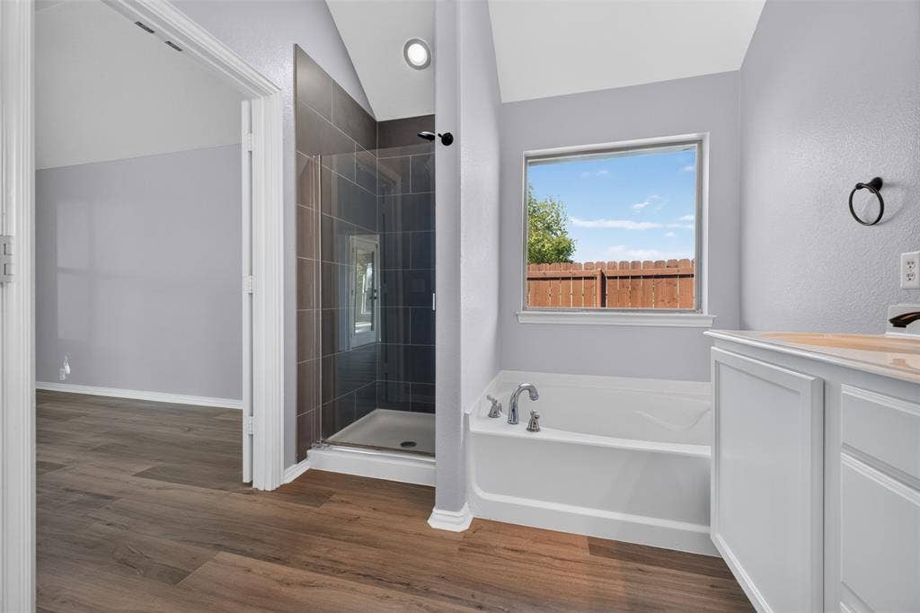 701 Abbey Lane, Midlothian, TX 76065 Bathroom featuring a glass-enclosed shower with tiled surround, a deep soaking tub, wood-finish flooring, and a vaulted ceiling