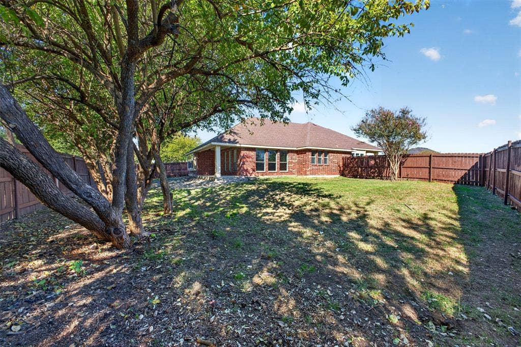 701 Abbey Lane, Midlothian, TX 76065 Backyard featuring a red brick exterior, mature trees, wood privacy fencing, and a covered patio