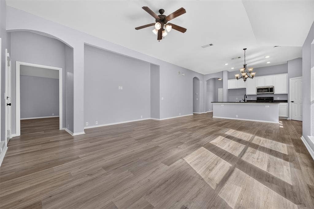 701 Abbey Lane, Midlothian, TX 76065 Open-concept living space featuring wood-finish flooring, high ceilings with recessed lighting, an architectural arched entry, a ceiling fan with integrated lighting, and a multi-tiered chandelier
