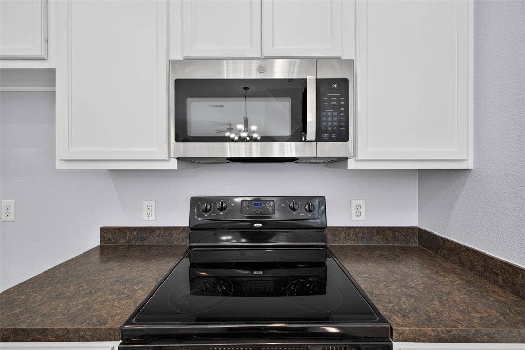 701 Abbey Lane, Midlothian, TX 76065 Kitchen featuring white cabinetry, dark countertops, and stainless steel microwave paired with a black glass-top range
