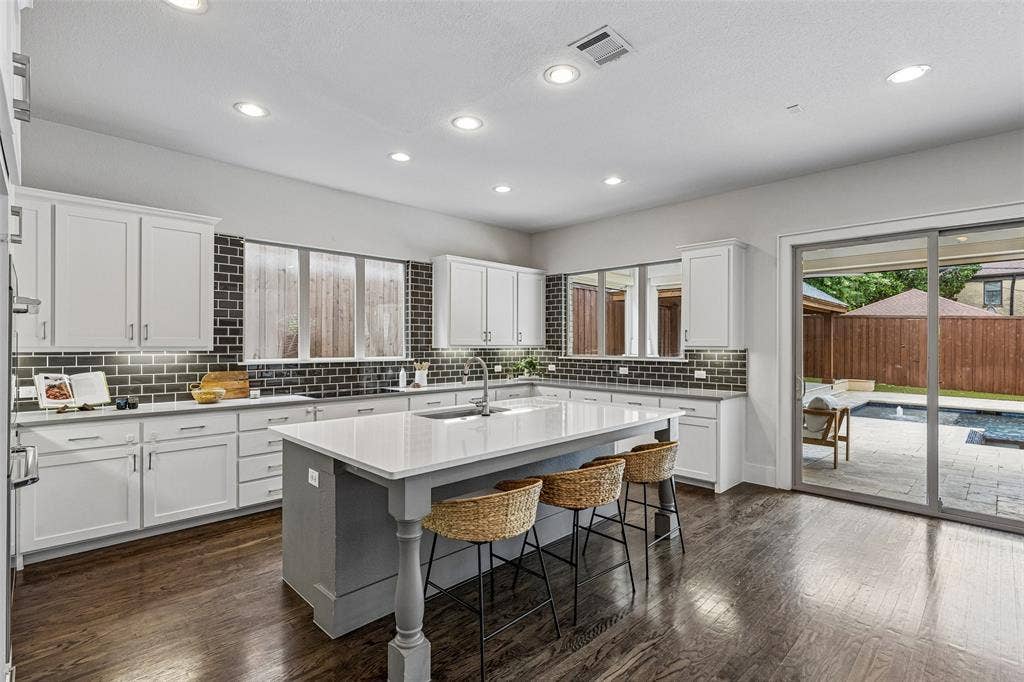 Kitchen featuring white cabinetry, a center island with a contrasting base and light-toned countertop, dark subway tile backsplash, wood-finish flooring, and recessed lighting