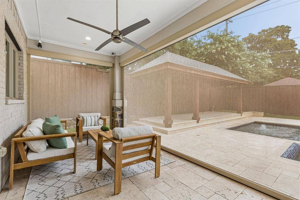 Covered patio featuring stone tile flooring, a mounted ceiling fan, retractable sun screening, and stone pillar accents, opening to a pool and custom gazebo