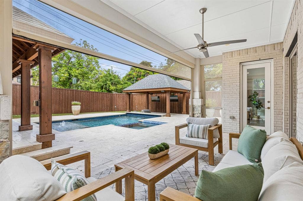 Covered patio featuring stone tile flooring, a ceiling fan, and a retractable screen, overlooking a swimming pool with an attached spa and a wooden pergola