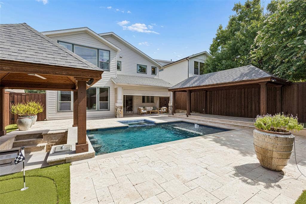 Backyard oasis featuring an in-ground pool with an integrated spa, stone-paver hardscaping, dual wood-post covered patios, and a synthetic turf putting green
