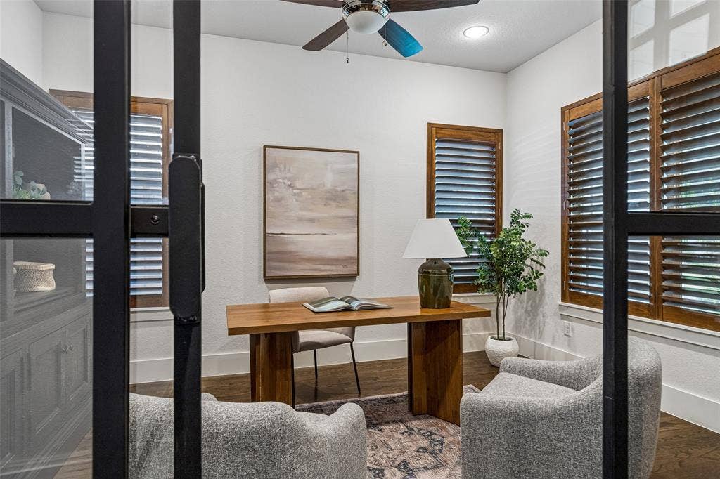 Interior room featuring black-framed glass partition doors, wood-finish flooring, plantation shutters, and a ceiling fan