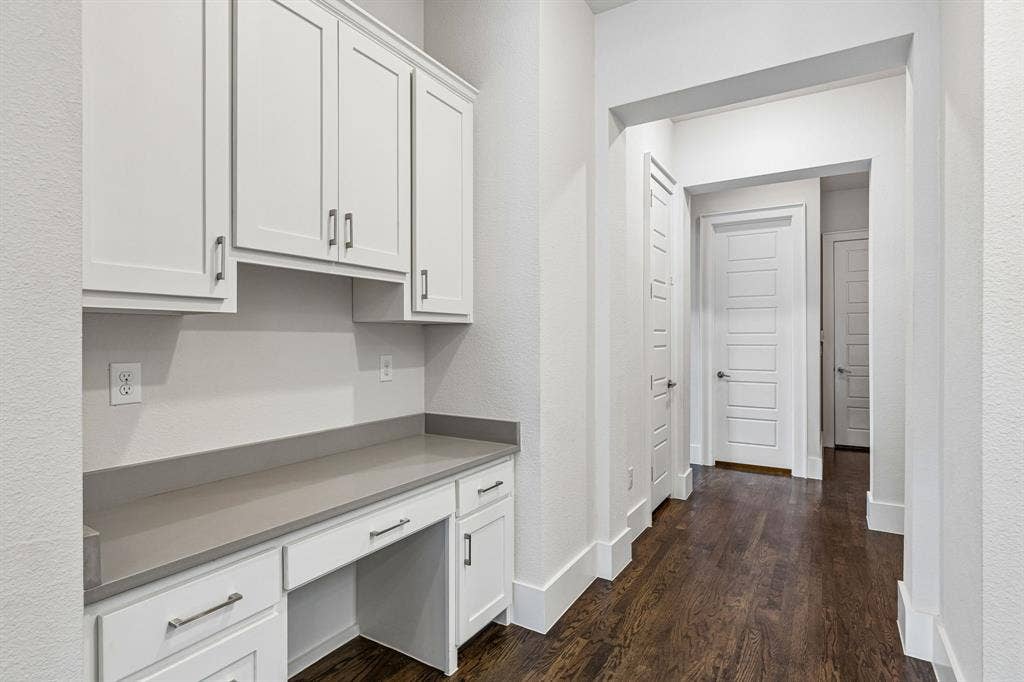 Built-in white cabinetry with shaker-style doors, solid-surface countertop, dark wood-finish flooring, and multi-panel interior doors