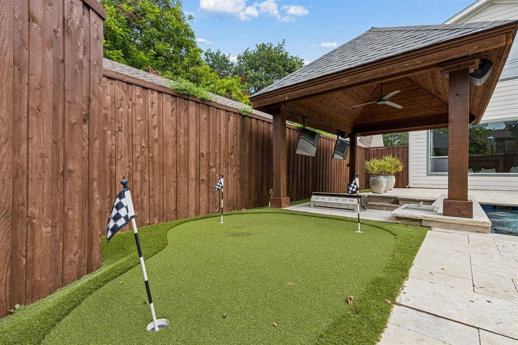 Backyard putting green featuring synthetic turf, surrounded by a wood privacy fence and a stone paver patio