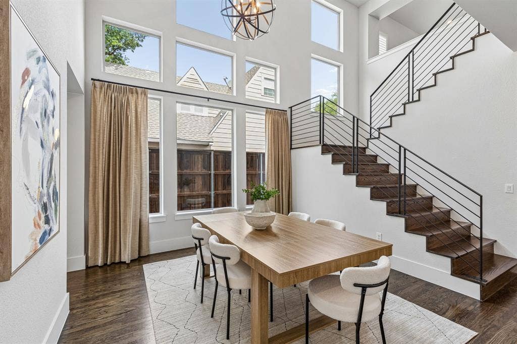 Double-height ceiling featuring multi-tiered windows, wood-finish flooring, and a staircase with a horizontal metal railing