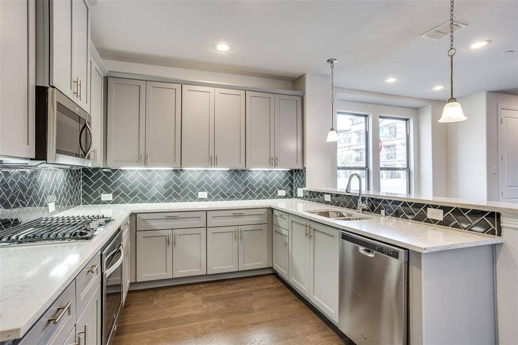 6341 Fortuna Lane, McKinney, TX 75070 Kitchen featuring light-toned cabinetry, herringbone-patterned tile backsplash, stone-finish countertops, stainless steel appliances, and wood-finish flooring
