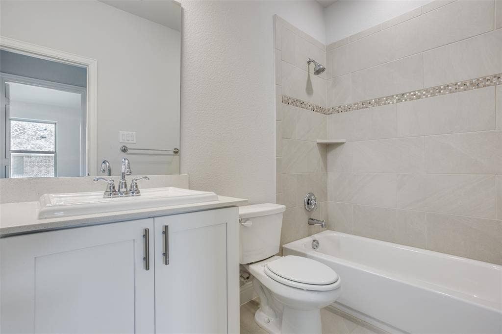6341 Fortuna Lane, McKinney, TX 75070 White vanity with a rectangular sink, polished chrome widespread faucet, large wall-mounted mirror, and a tub-shower combination featuring horizontal tile surrounds with a decorative mosaic inlay