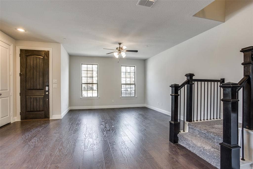 6341 Fortuna Lane, McKinney, TX 75070 Interior space featuring dark wood-finish flooring, two multi-pane windows, a ceiling fan with integrated lighting, and a staircase with a dark-finished handrail and metal balusters