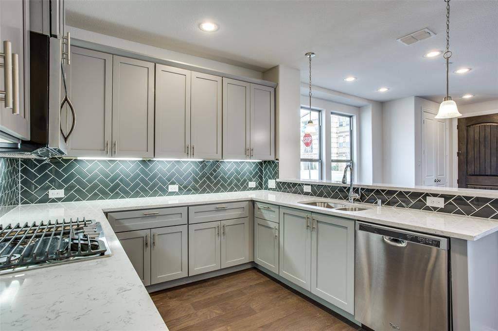 6341 Fortuna Lane, McKinney, TX 75070 Kitchen featuring shaker-style cabinetry, quartz countertops, herringbone-pattern tile backsplash, stainless steel appliances, and wood-finish flooring