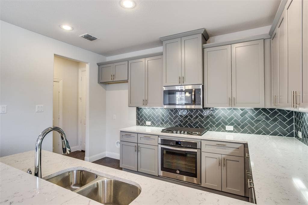 6341 Fortuna Lane, McKinney, TX 75070 Kitchen featuring grey shaker-style cabinetry, white countertops with grey veining, a herringbone-patterned tile backsplash, stainless steel appliances, and a double-basin undermount sink with a pull-down faucet